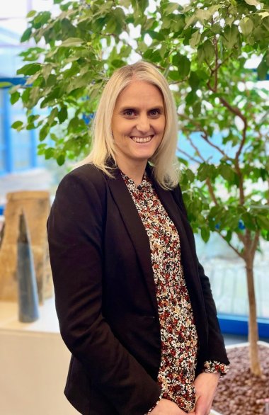 lächelnde blonde Frau vor Fikus-Baum