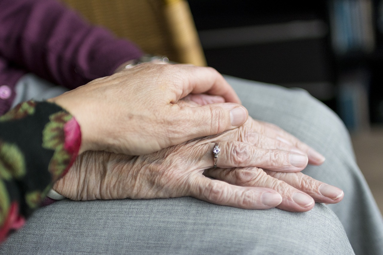 Hand liegt tröstend auf zwei Händen einer älteren Person