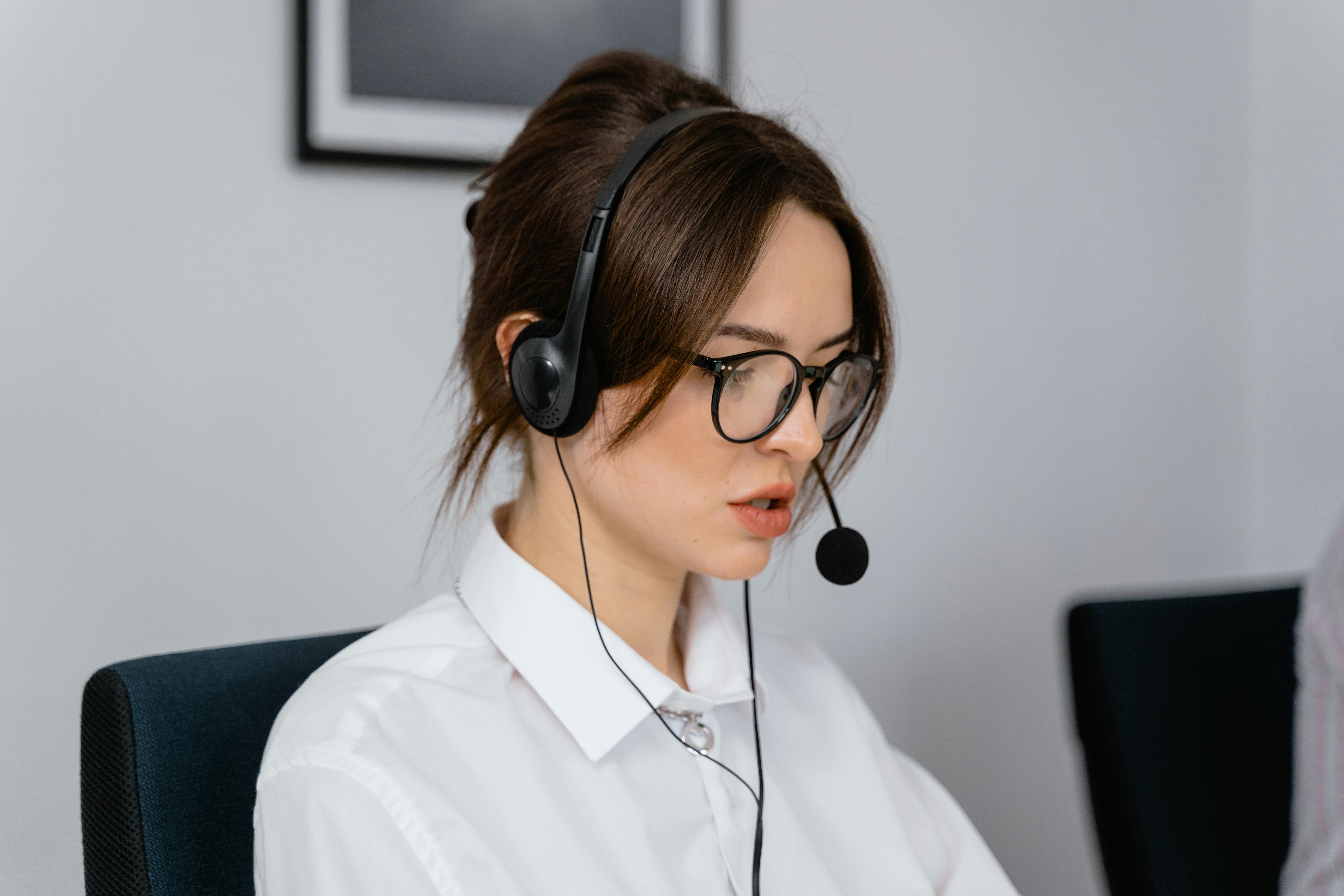 mit Headset am PC dunkelhaarige Frau mit weißer Bluse sitzt mit Headset am Computer