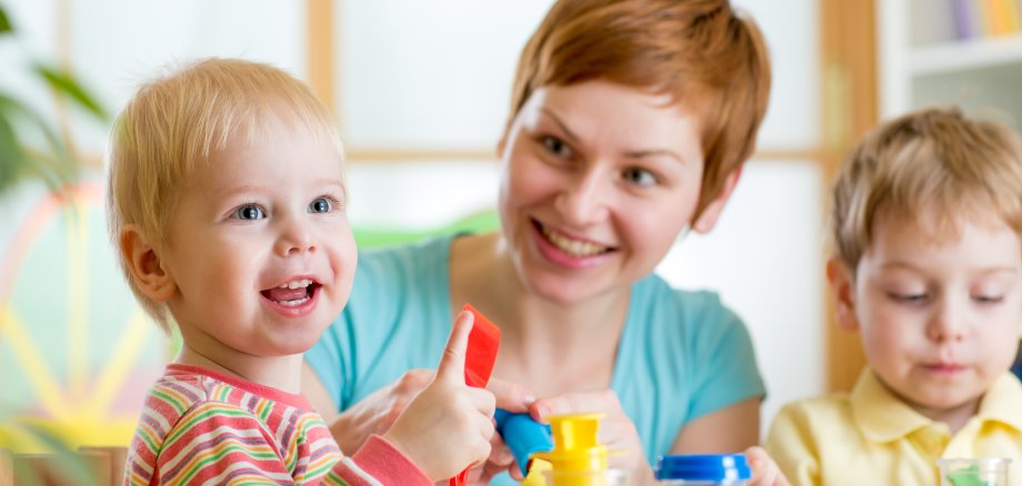 kurzhaarige Frau spielt mit zwei blonden Kleinkindern am Tisch