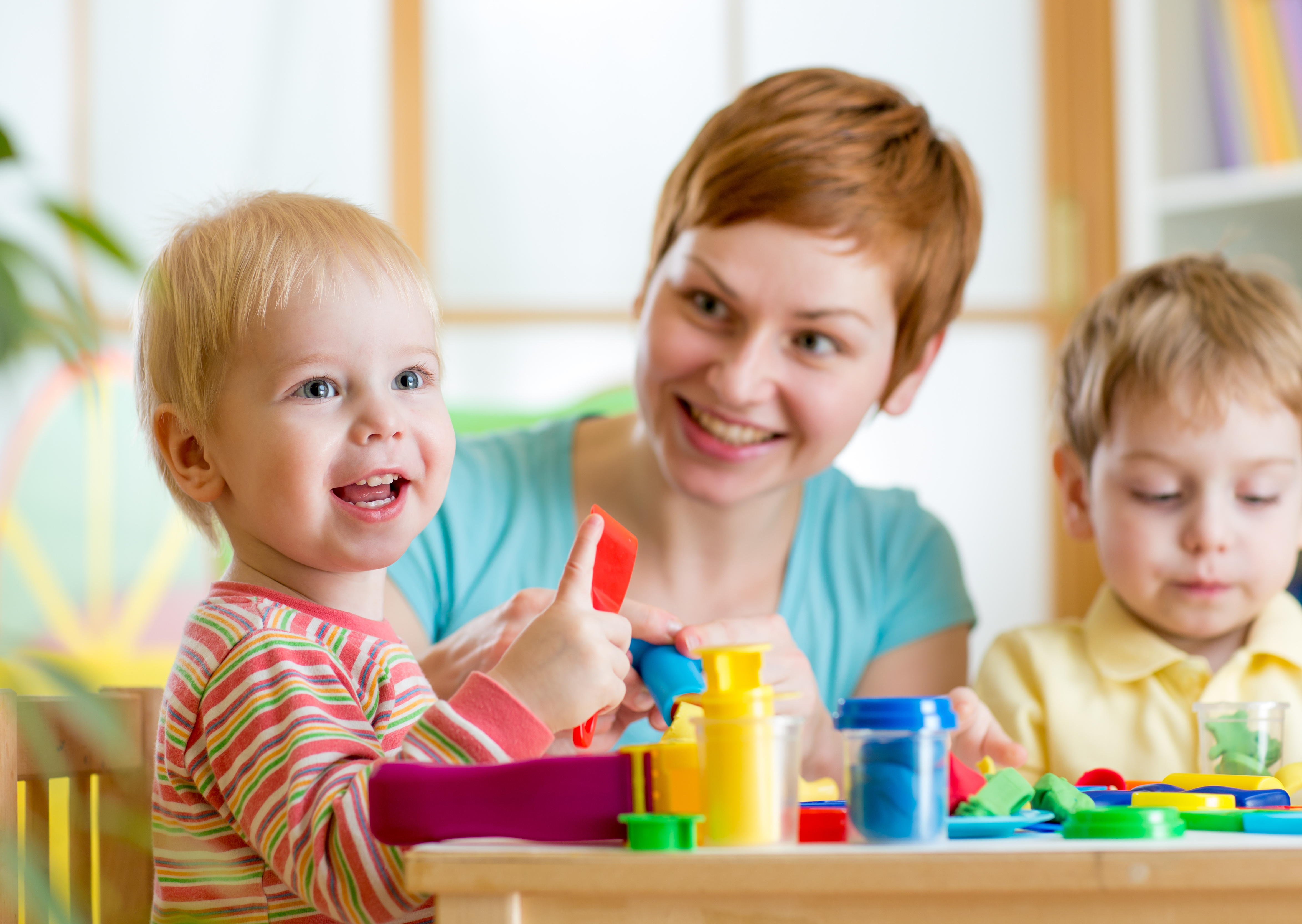 kurzhaarige Frau spielt mit zwei blonden Kleinkindern am Tisch