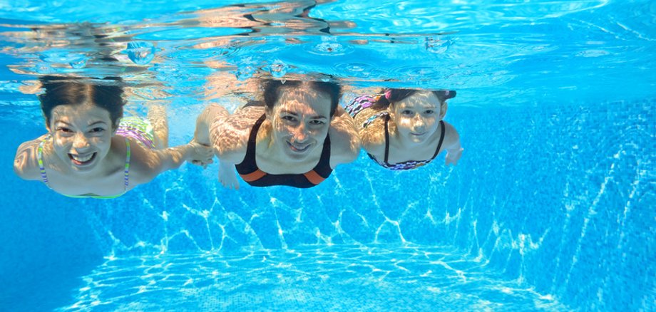 Tauchen im Schwimmbad Frau taucht mit zwei Kindern im Schwimmbecken