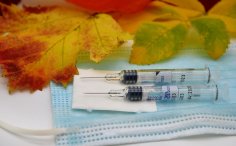 Foto mit zwei Spritzen auf einer medizinischen Maske und zwei bunten Herbstblättern im oberen Drittel des Bildes